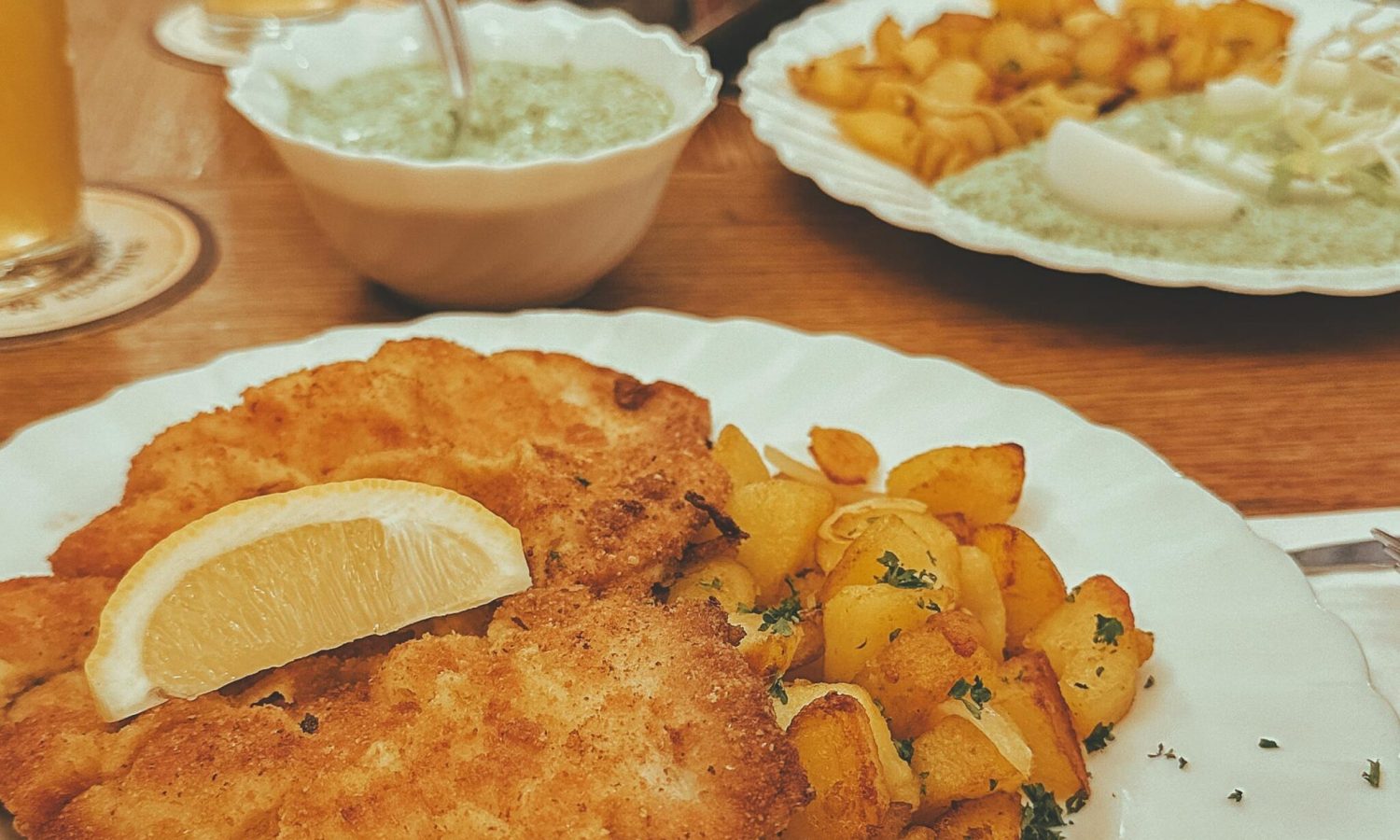 Delicious crispy schnitzel with golden potatoes and refreshing drinks on a wooden table.