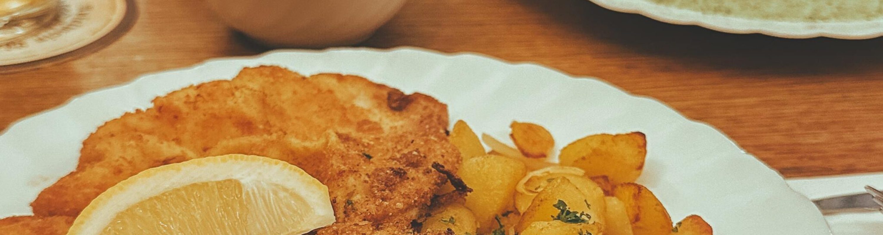 Delicious crispy schnitzel with golden potatoes and refreshing drinks on a wooden table.